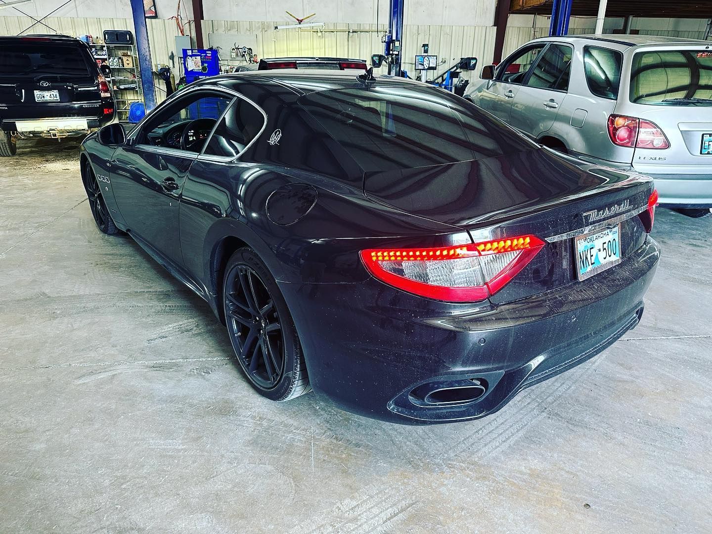A black car is parked in a garage with other cars.