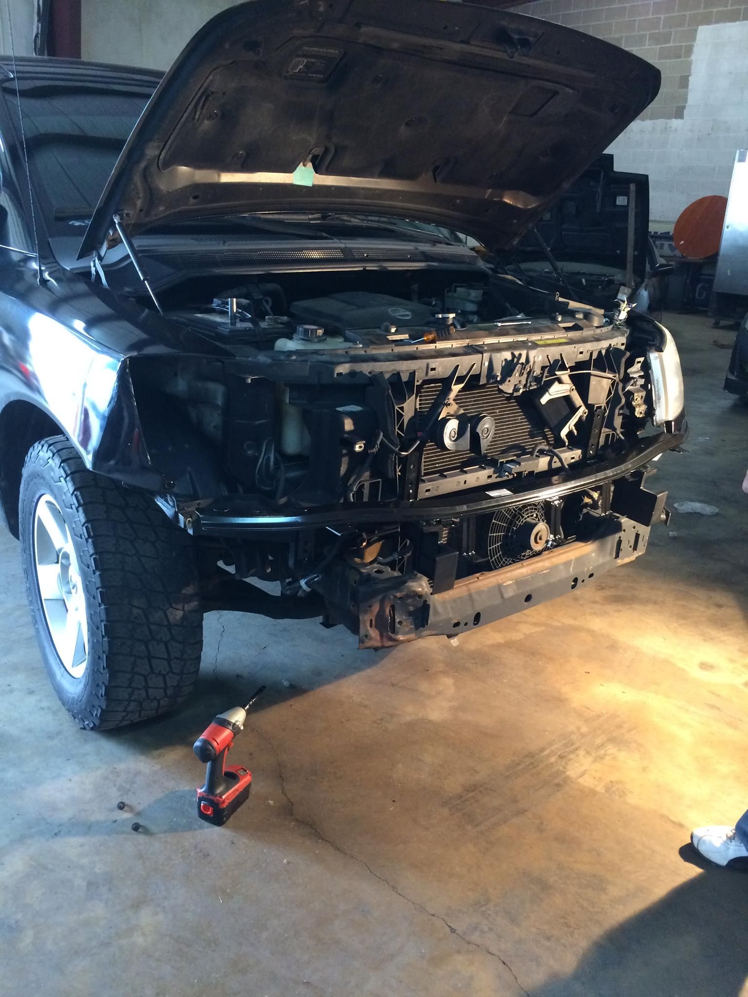 A black truck with the hood open is being worked on in a garage.