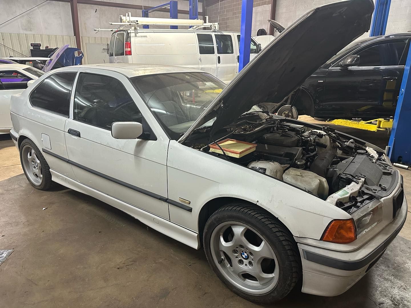 A white car with the hood open is parked in a garage.
