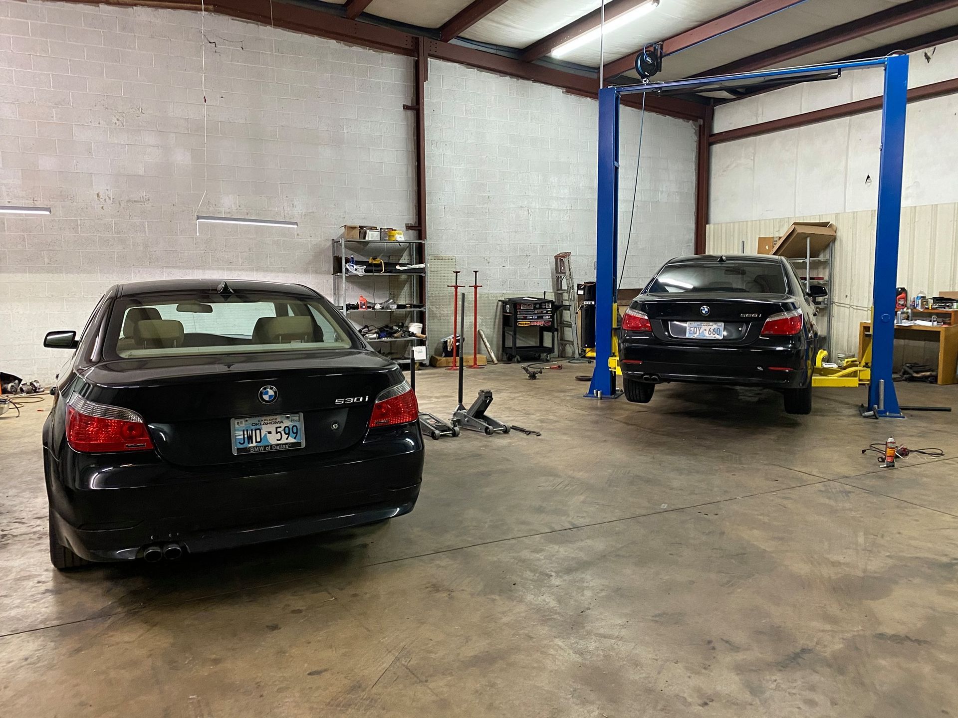 Two cars are parked in a garage on a lift.