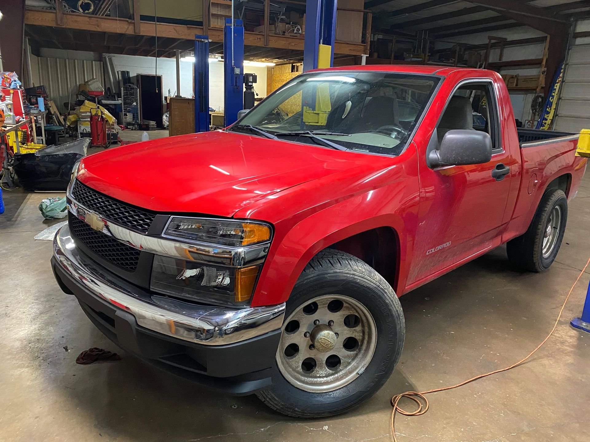 A red truck is parked in a garage next to a lift.