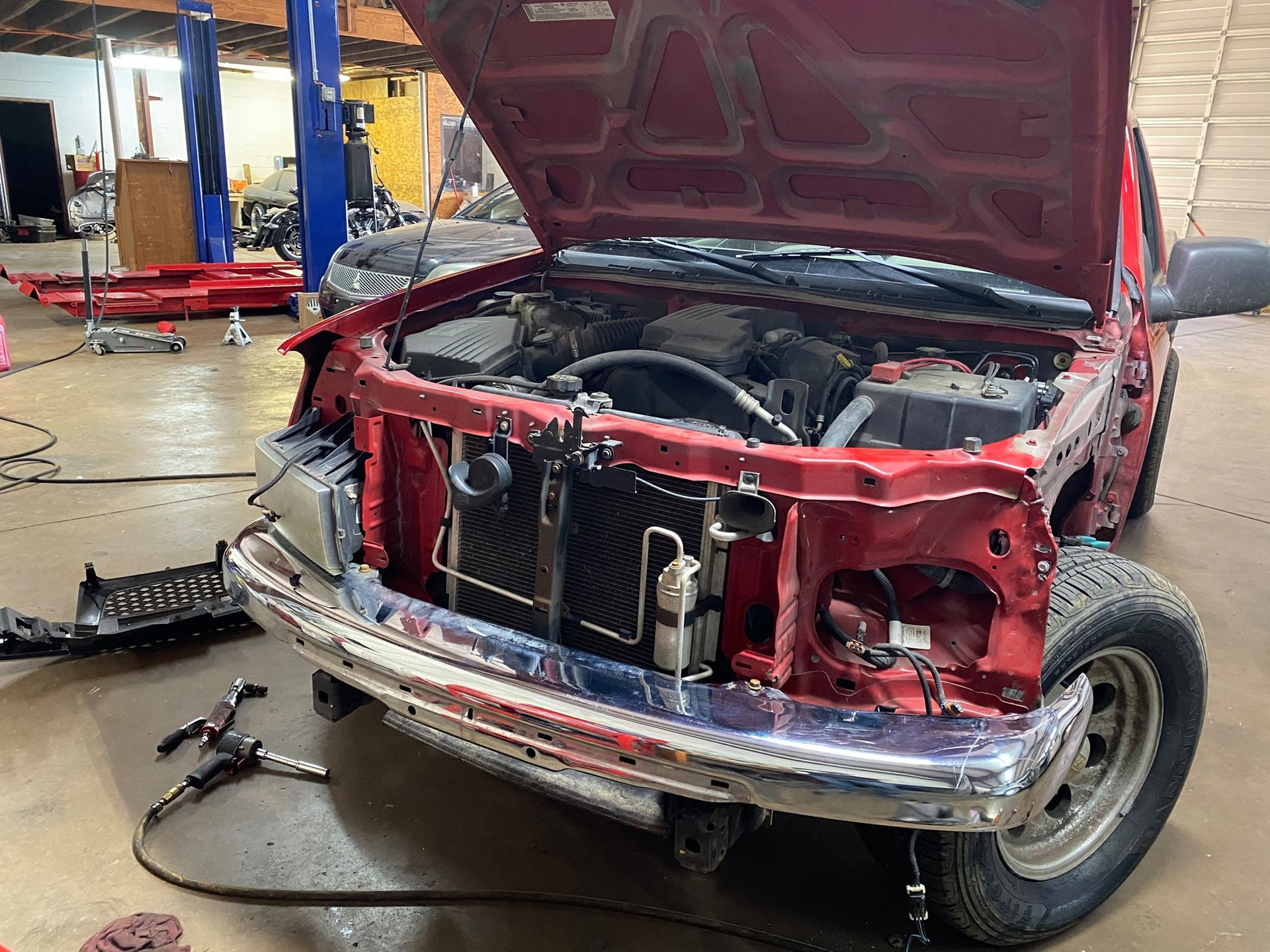 A red truck with the hood up is being worked on in a garage.