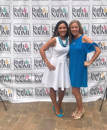 Two women are posing for a picture in front of a banner that says ruth & naomi.