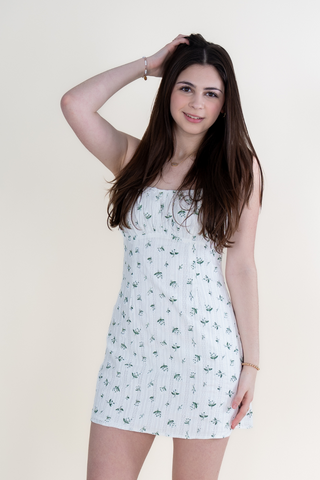 A woman in a white dress is standing in front of a white wall.