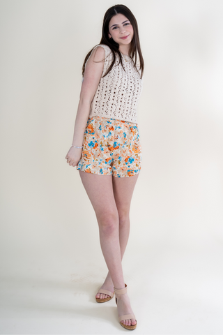 A woman is wearing a white top and floral shorts.