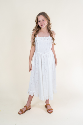 A young girl is wearing a white dress and brown sandals.