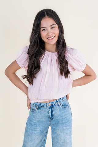 A young girl is wearing a pink crop top and blue jeans.