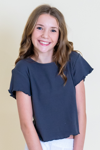 A young girl wearing a black crop top and white shorts is smiling.