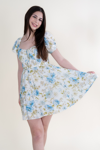 A woman in a white floral dress is standing on a white background.