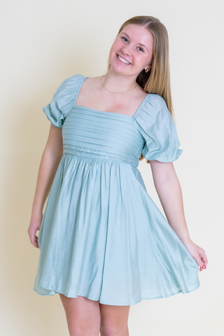 A woman is wearing a light blue dress and smiling.