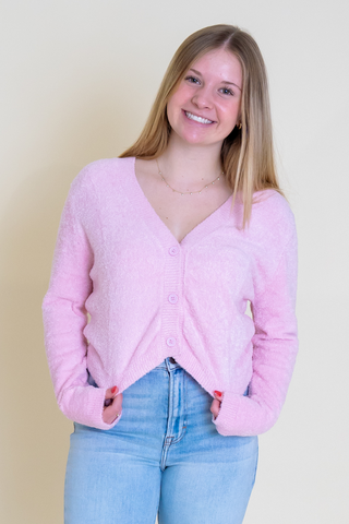 A woman is wearing a pink cardigan and blue jeans.