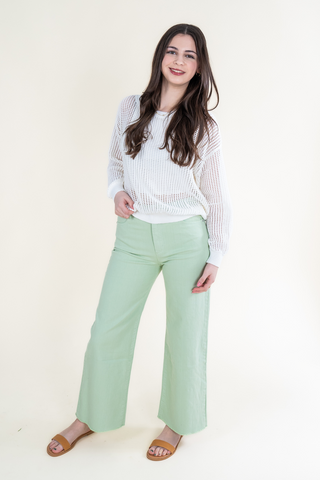 A woman is wearing a white blouse and green pants.
