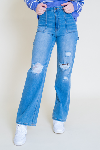 A woman is wearing a purple sweater and wide leg jeans.