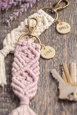 A macrame keychain is sitting on a wooden table next to a bunch of keys.