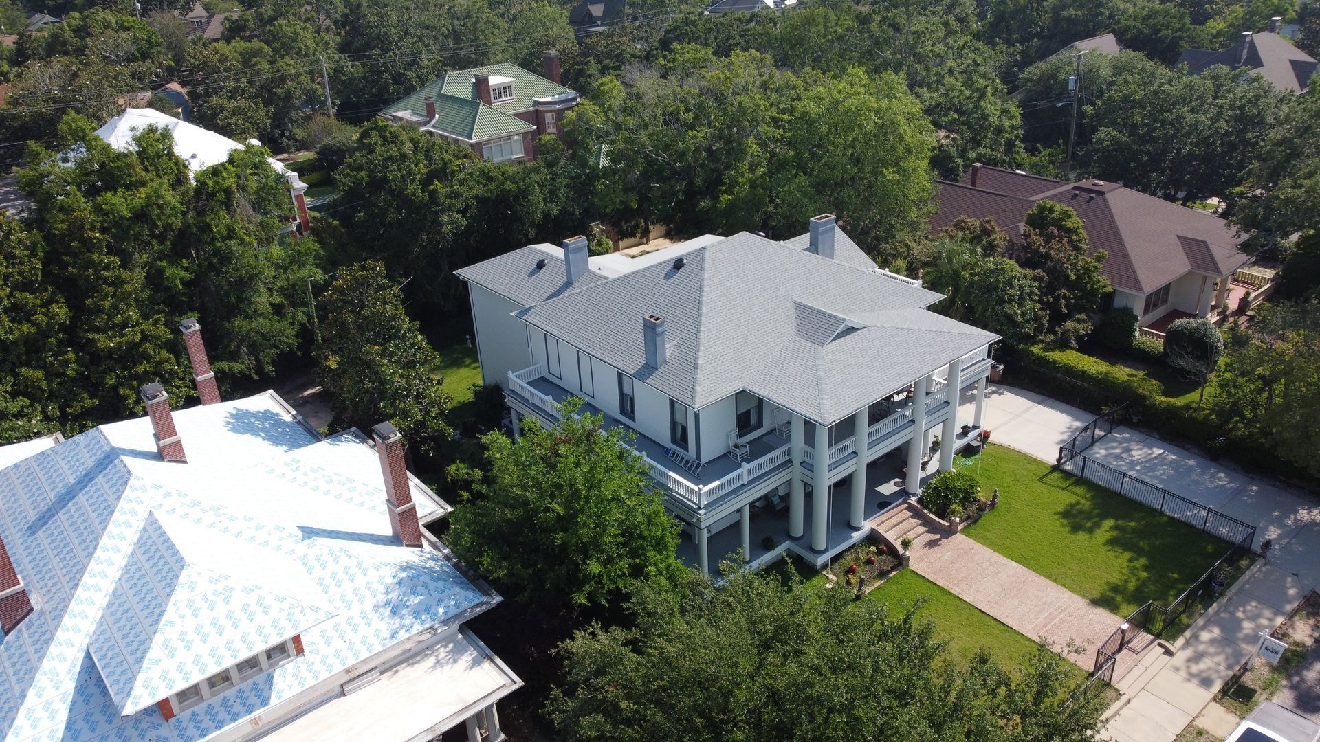 Aerial view of a two-story white house with a gray roof and porch surrounded by green trees.