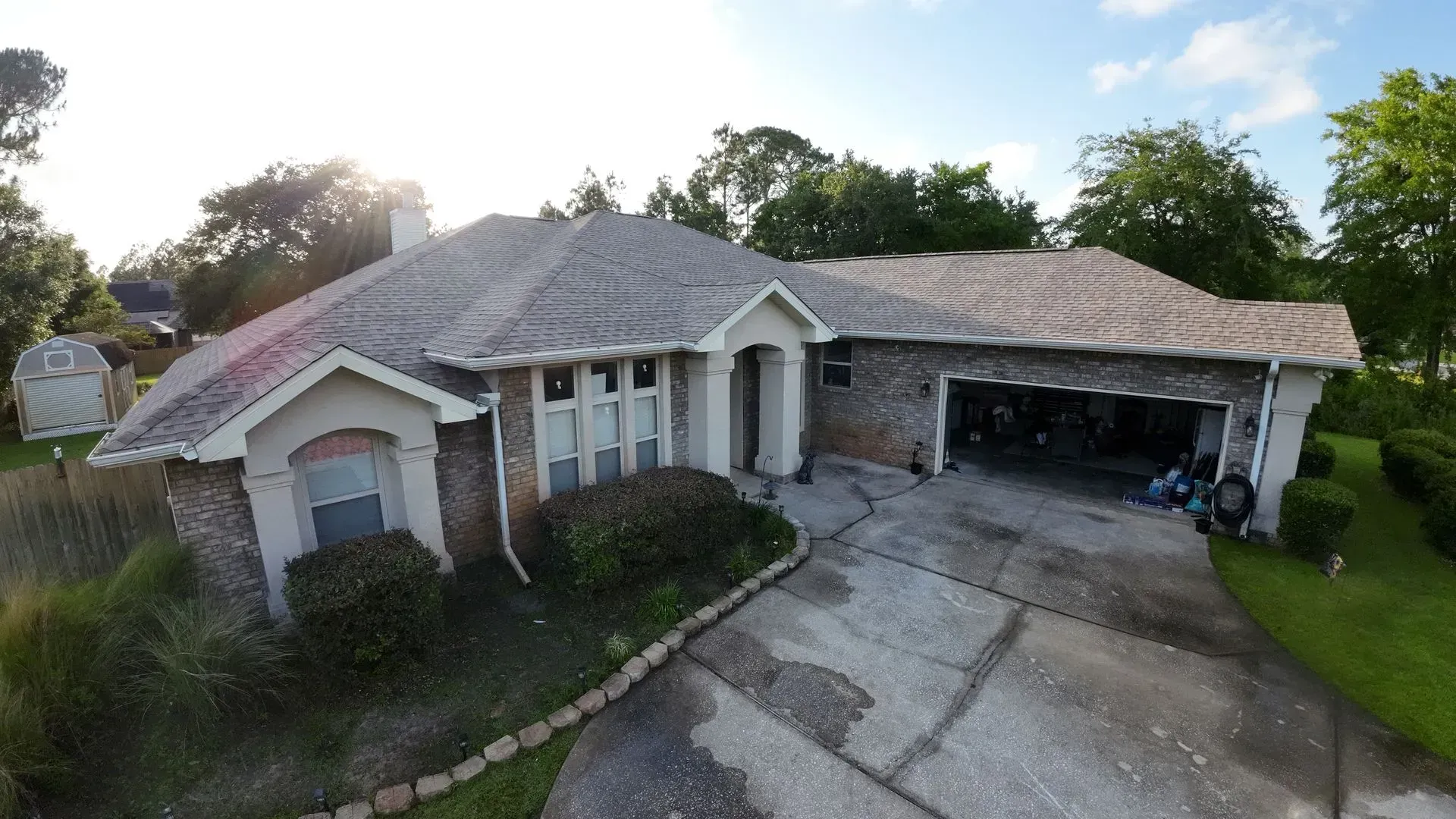 Single-story brick home with a garage and driveway on a sunny day; bushes and lawn surround the house.