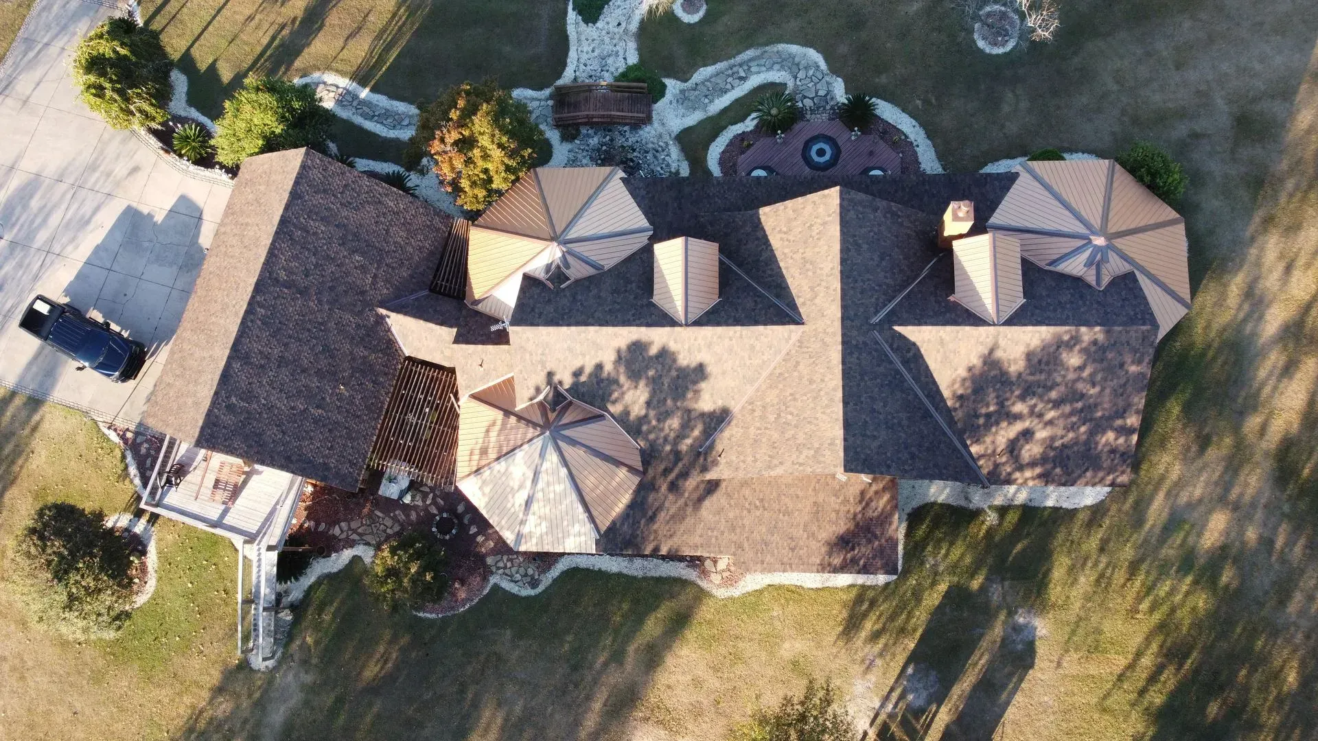Aerial view of a large house with a brown roof, landscaping, and a black truck in the driveway.