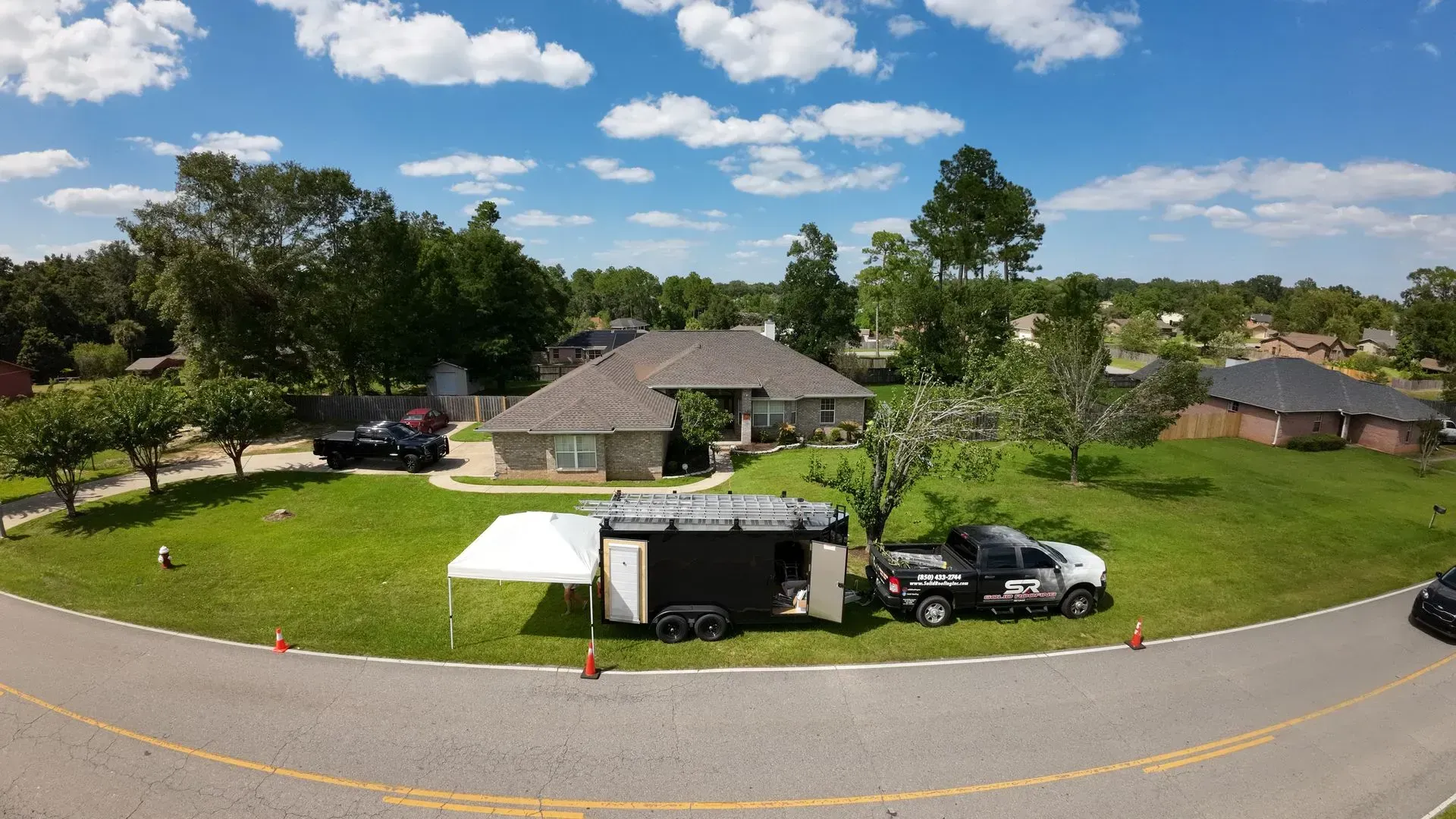 House with vehicles parked on the lawn and a tent, sunny day.