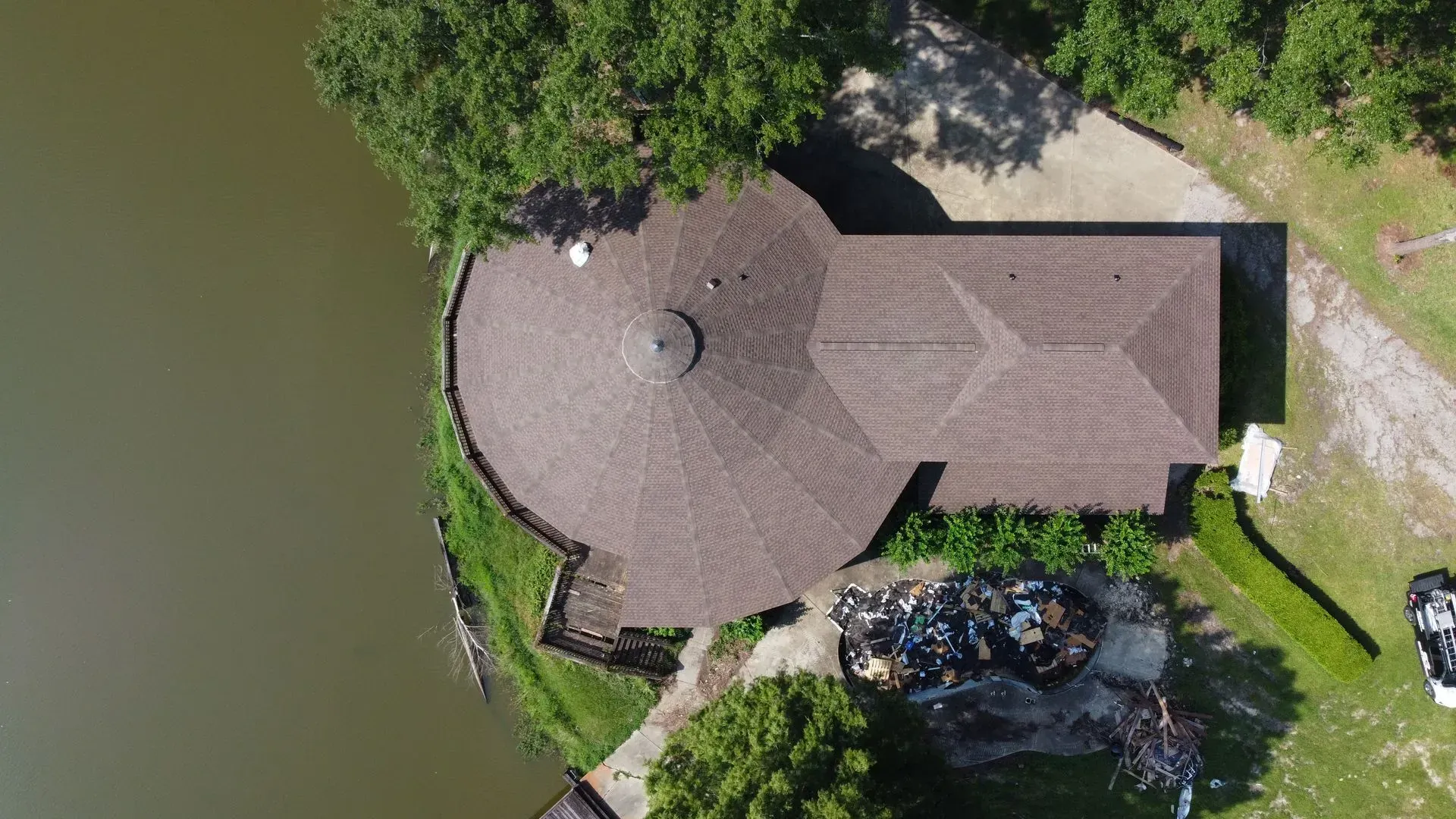 Overhead view of a circular building with a brown roof next to a body of water and green trees.