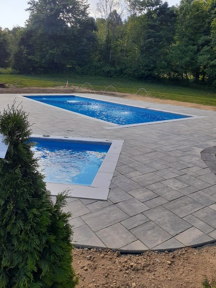 Two pools with blue water, surrounded by gray paving stones, set in a yard with trees.