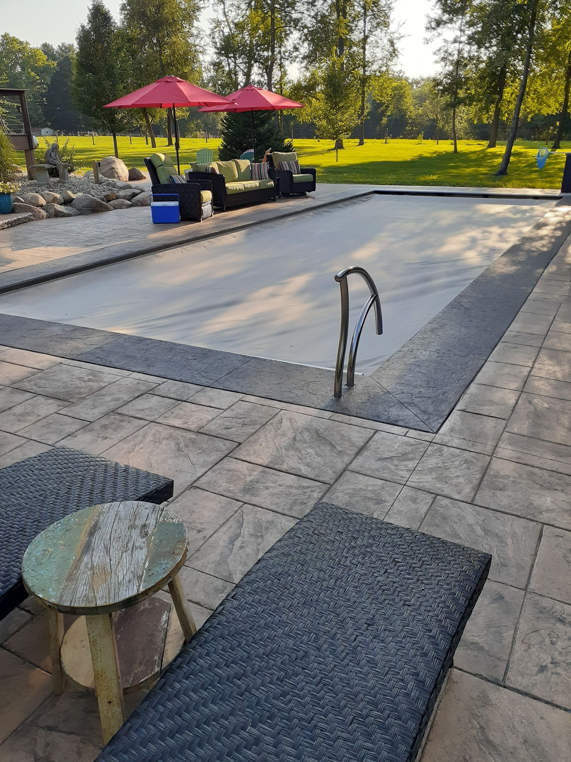 A large swimming pool is surrounded by a patio with chairs and umbrellas.