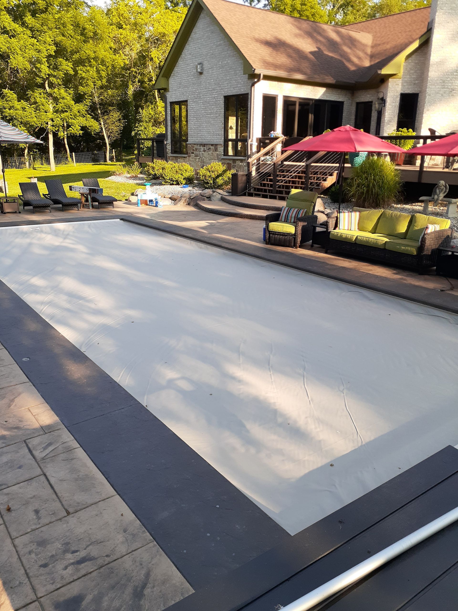 A large swimming pool surrounded by chairs and umbrellas in front of a house.