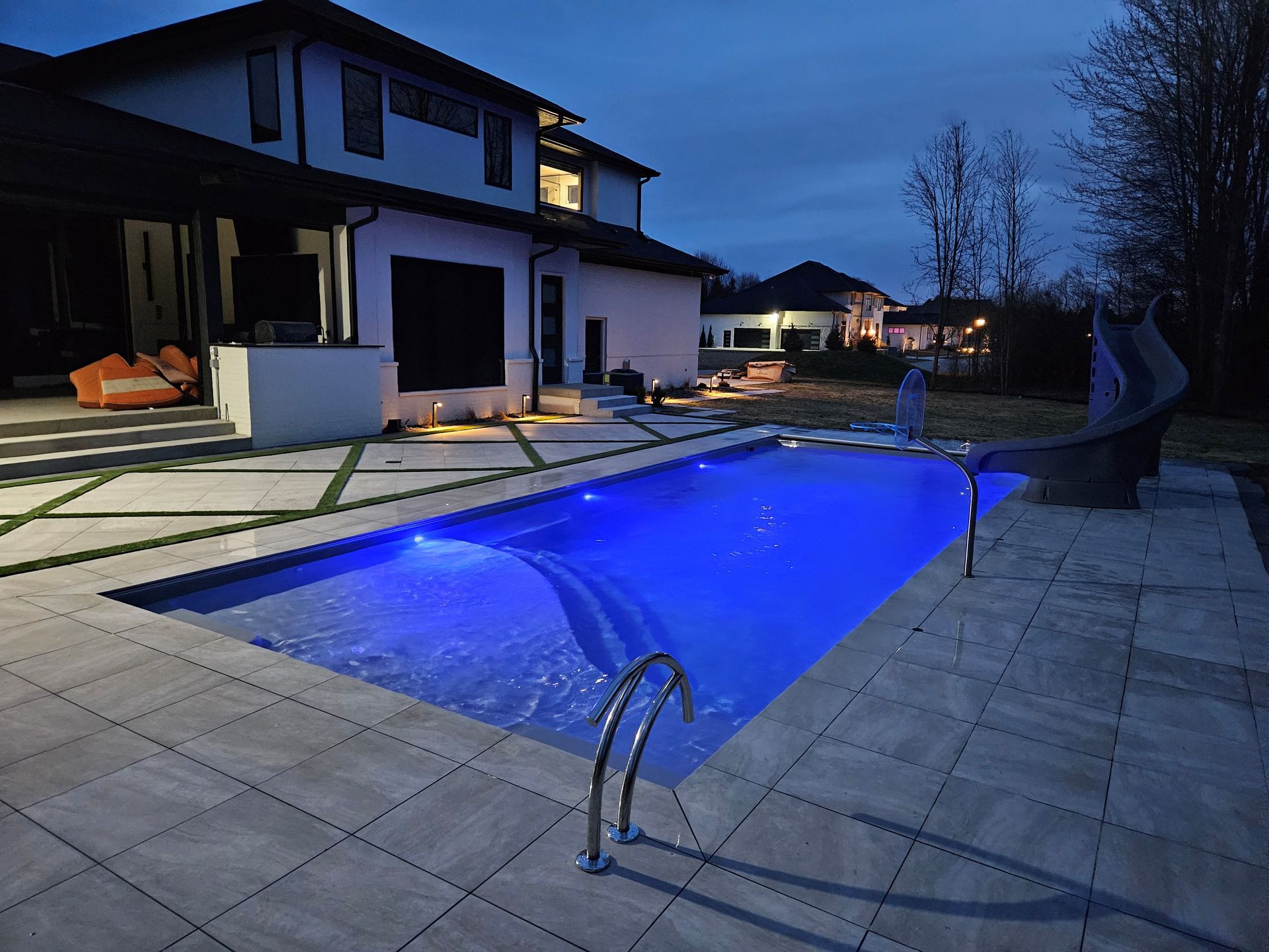 A large swimming pool is lit up at night in front of a house.