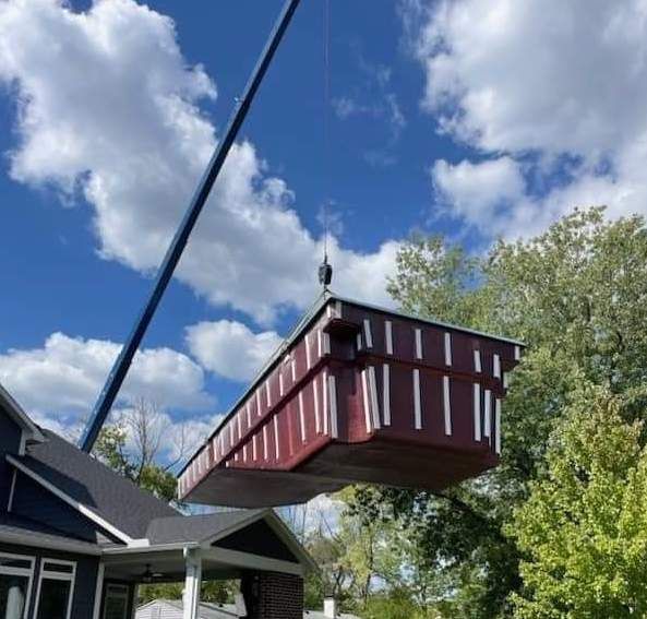 A large red box is being lifted by a crane over a house.