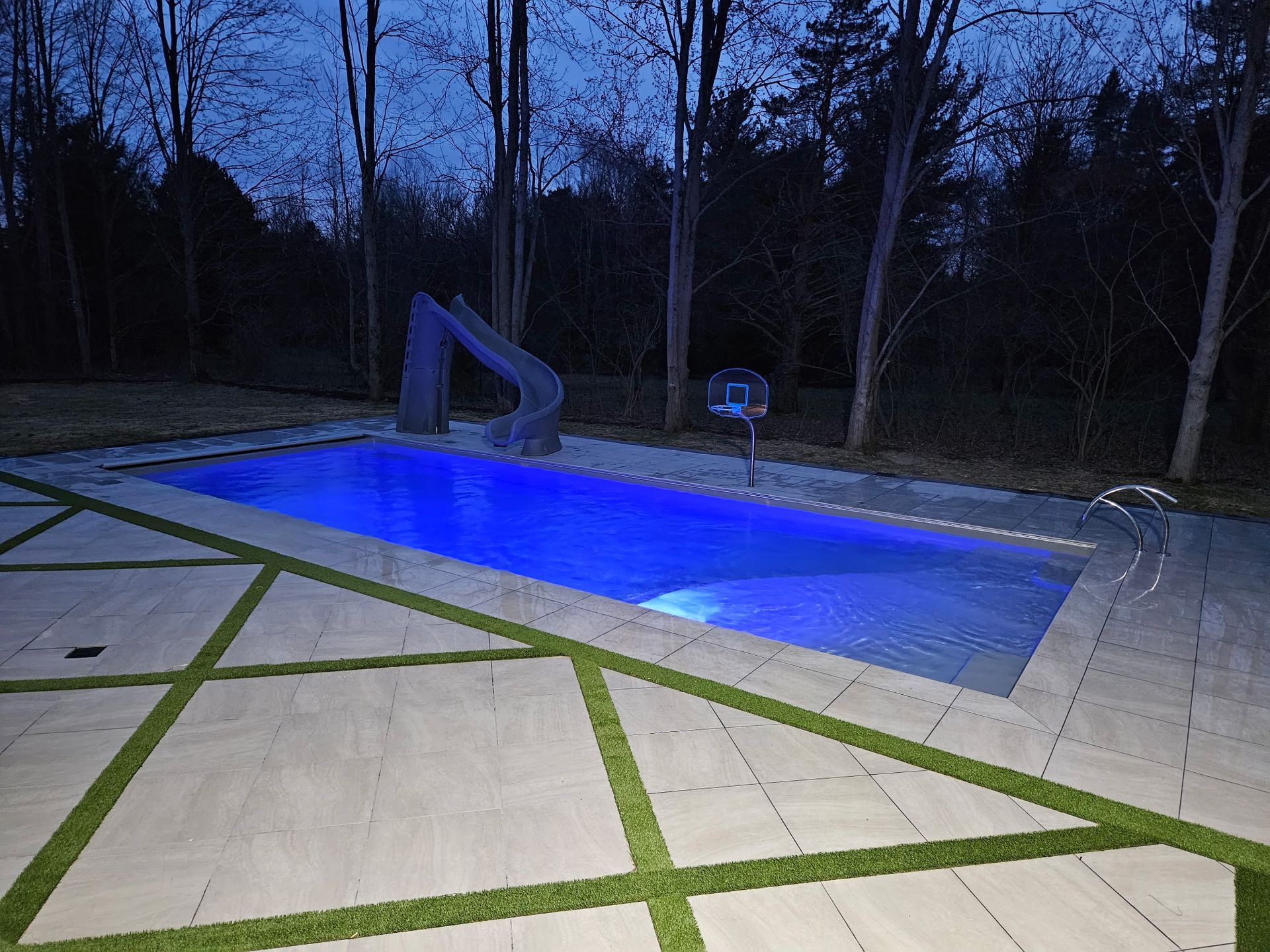 A large swimming pool with a slide in the backyard at night.
