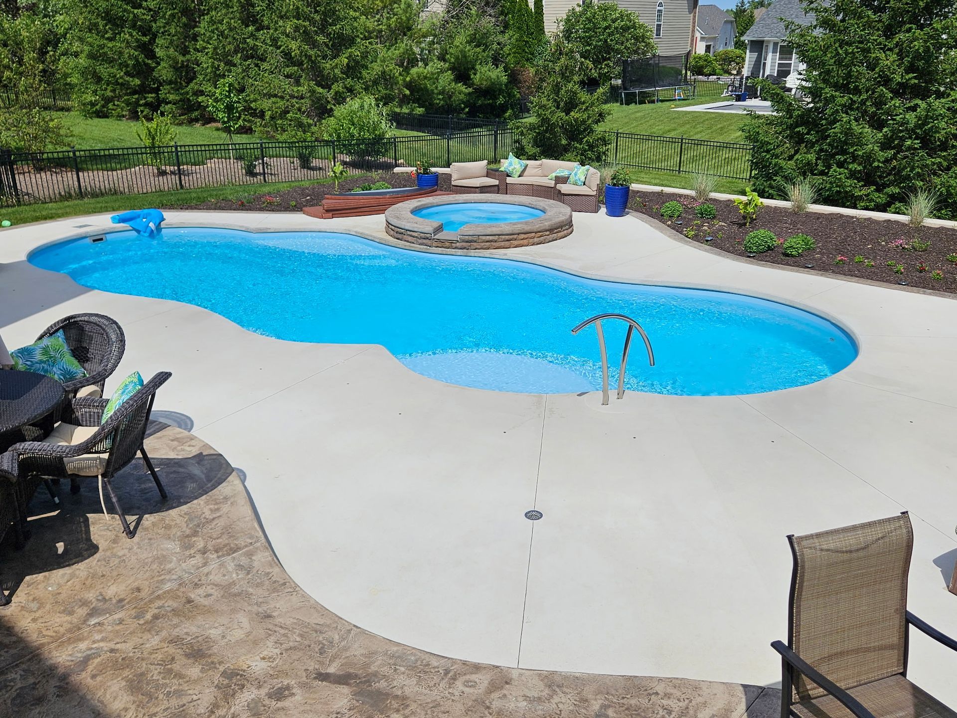A large swimming pool is surrounded by a patio and chairs.