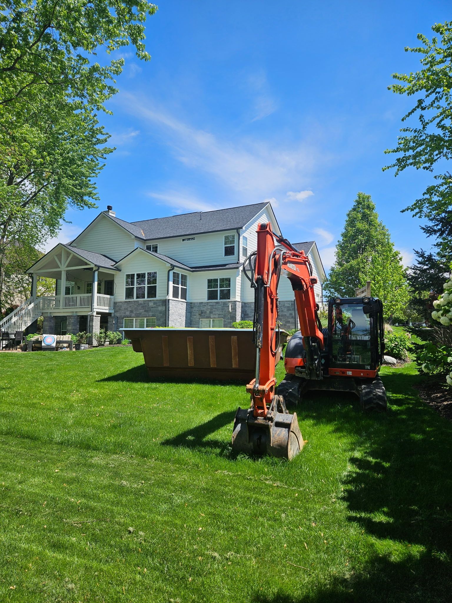 Mini excavator in a backyard, near a two-story white house with a blue sky.