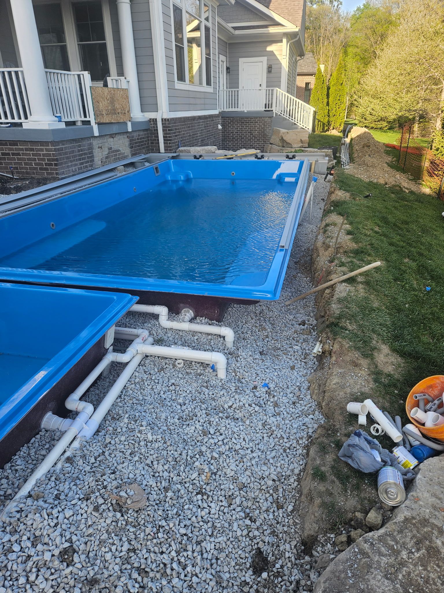 A rectangular blue pool being installed next to a house with white piping and gravel.