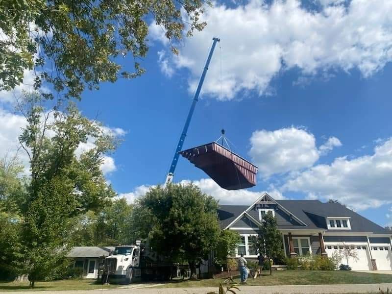 A crane lifts a large, red container over a house with a blue sky background.