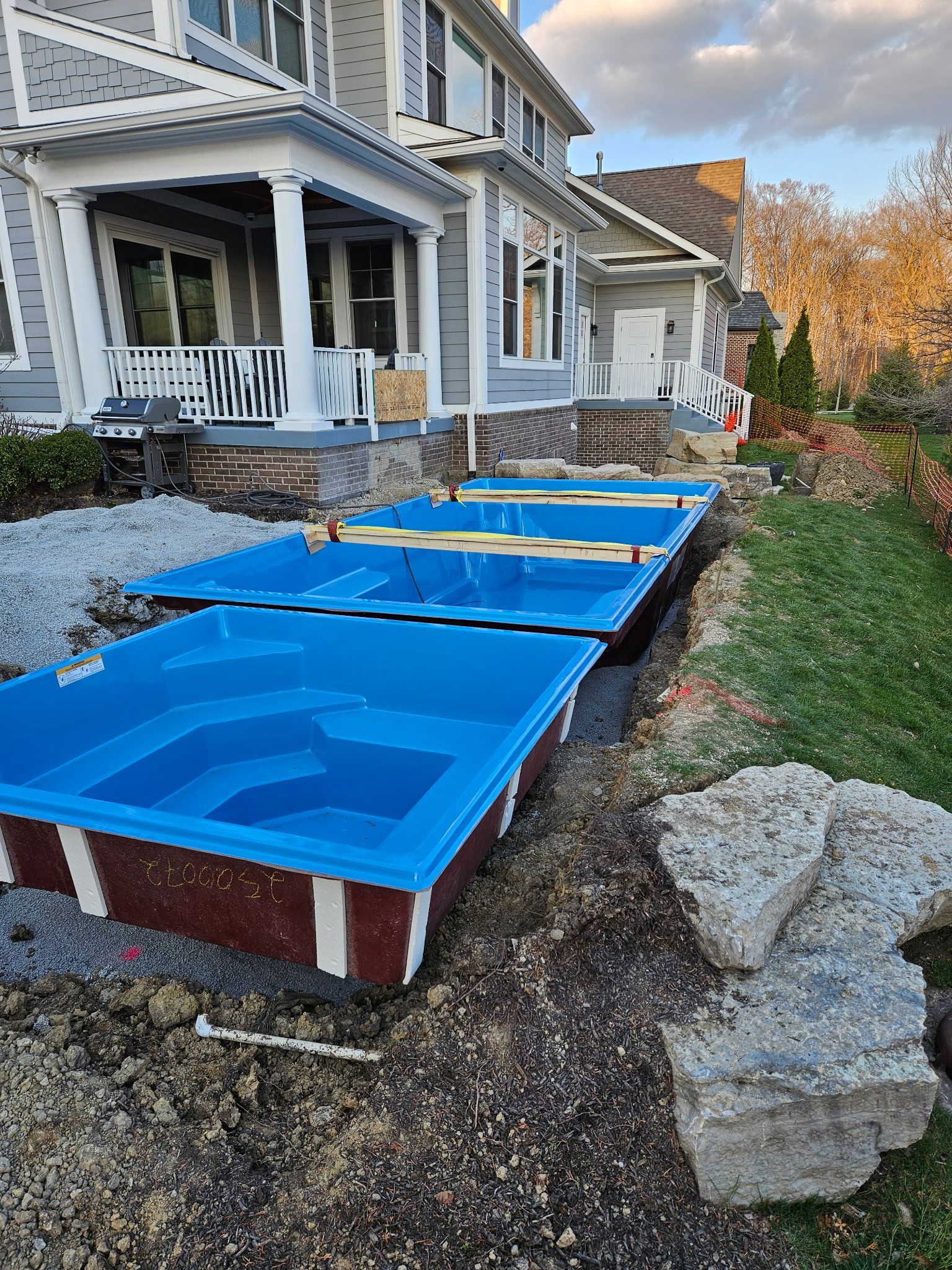 Blue pool forms set in excavated ground next to a light gray house under construction.