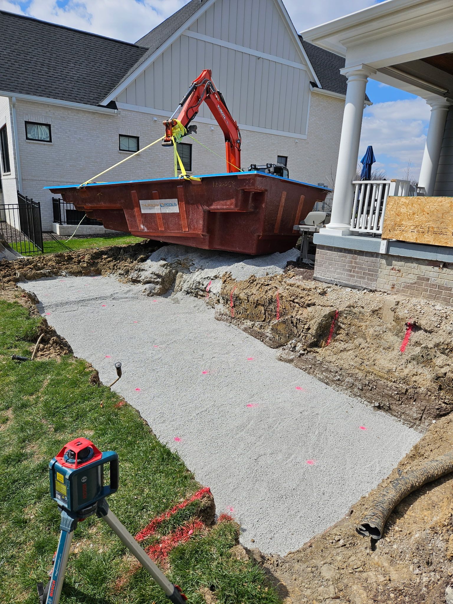Excavation site with a gravel base. An excavator and dumpster are in the backyard of a house under construction.