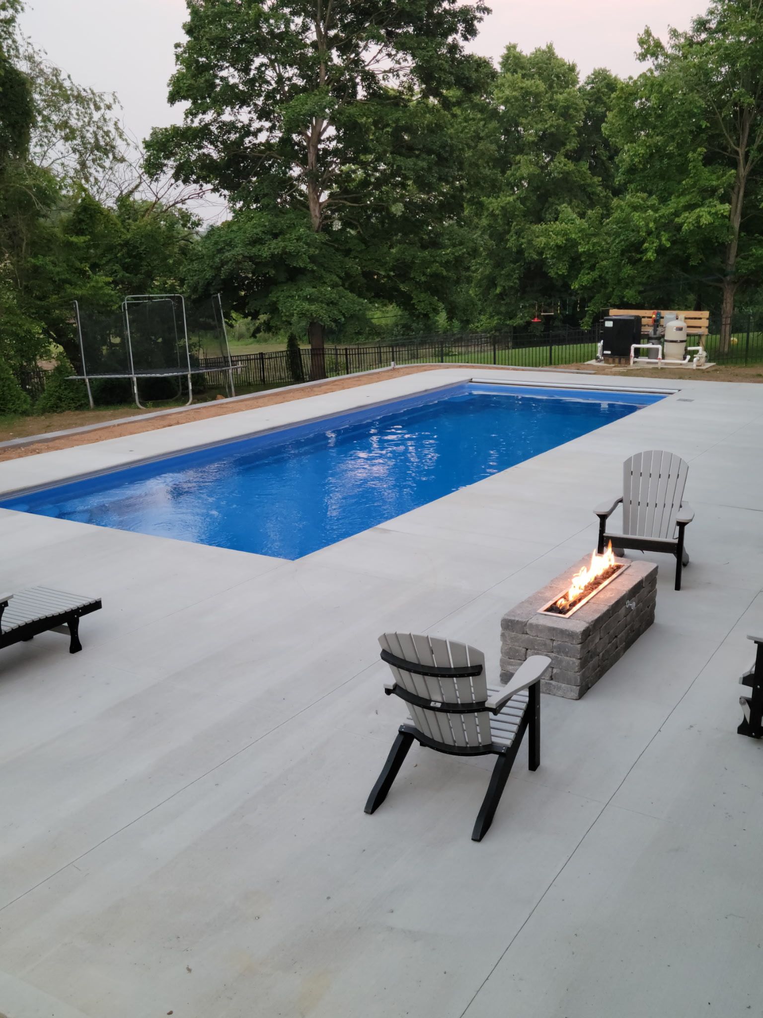 Outdoor pool with chairs, fire pit, and trees in background.