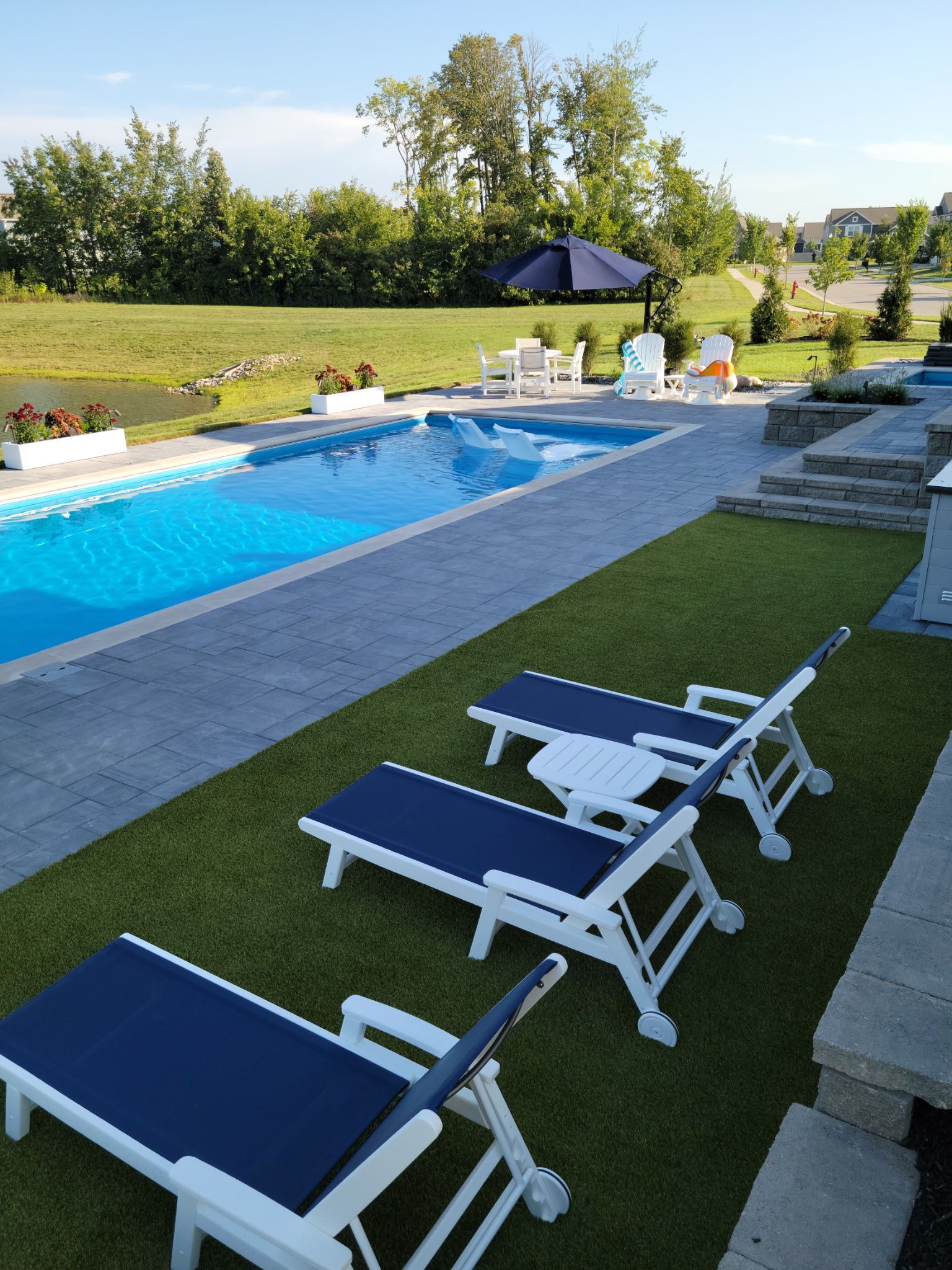 Poolside scene with pool, lounge chairs on artificial turf, umbrella, and a grassy landscape.