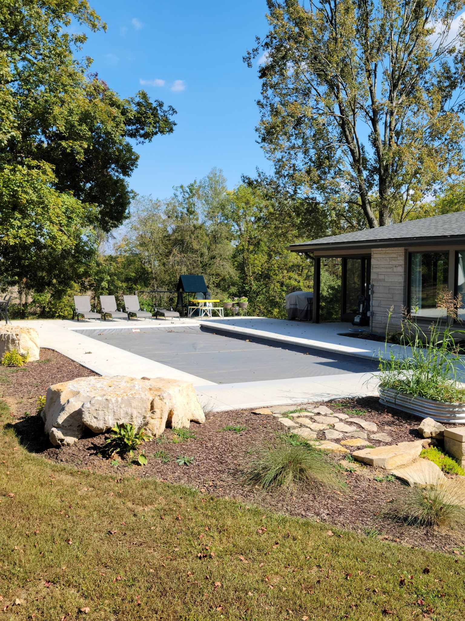 Backyard with pool, patio, and lush trees under a blue sky.