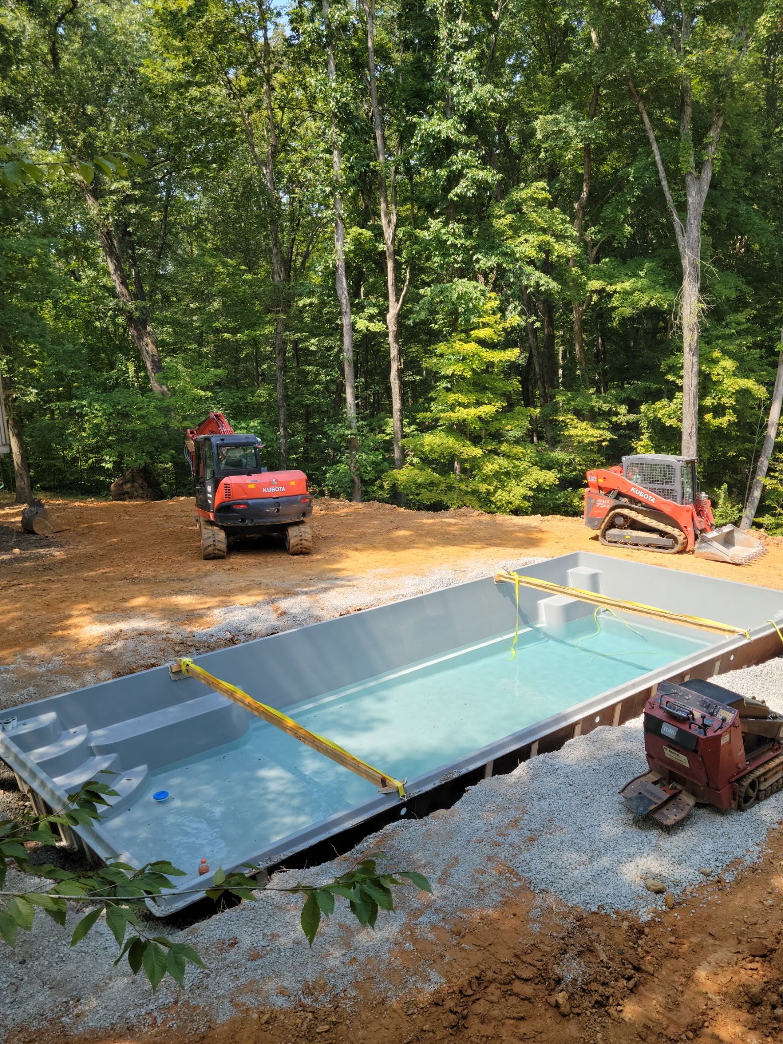 Pool installation site: Excavators surround a rectangular pool, setting in a wooded area.