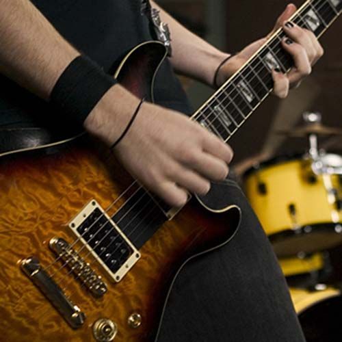 A man is playing an electric guitar in front of a drum set