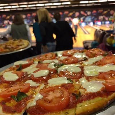 A pizza with tomatoes and cheese is sitting on a plate in front of a bowling alley.
