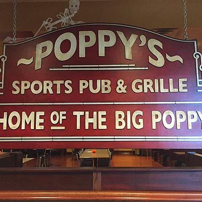 A sign for poppy 's sports pub and grille is hanging from the ceiling of a restaurant.