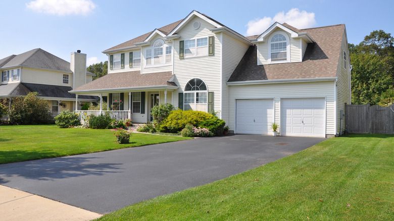 A white house with a brown roof and a black driveway