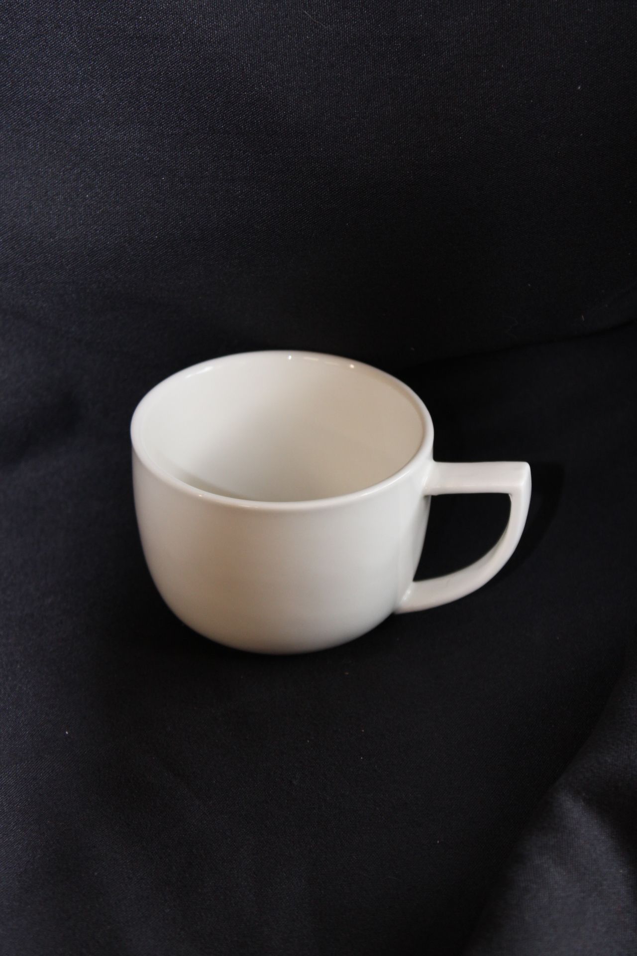 A white cup with a handle is sitting on a black cloth