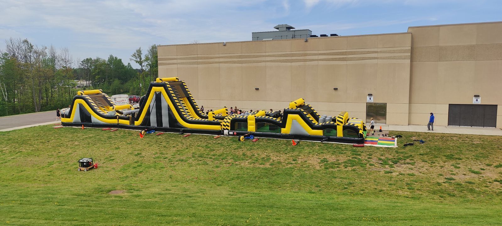 A large inflatable obstacle course is sitting in a grassy field in front of a building.