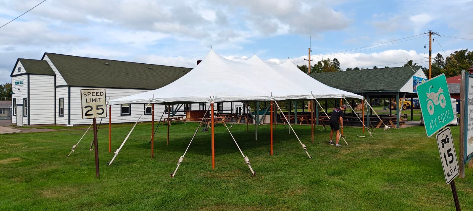 A large white tent is sitting in a grassy field in front of a house.
