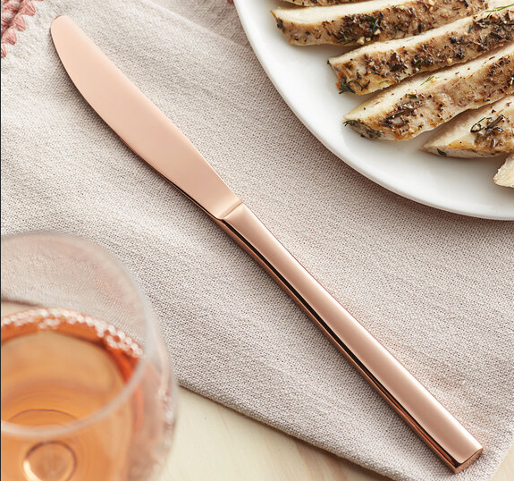 Rose gold knife on beige linen with sliced chicken and a glass of rosé.