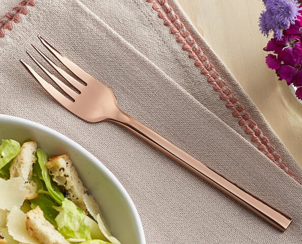 Rose gold fork on a beige napkin next to a salad bowl.