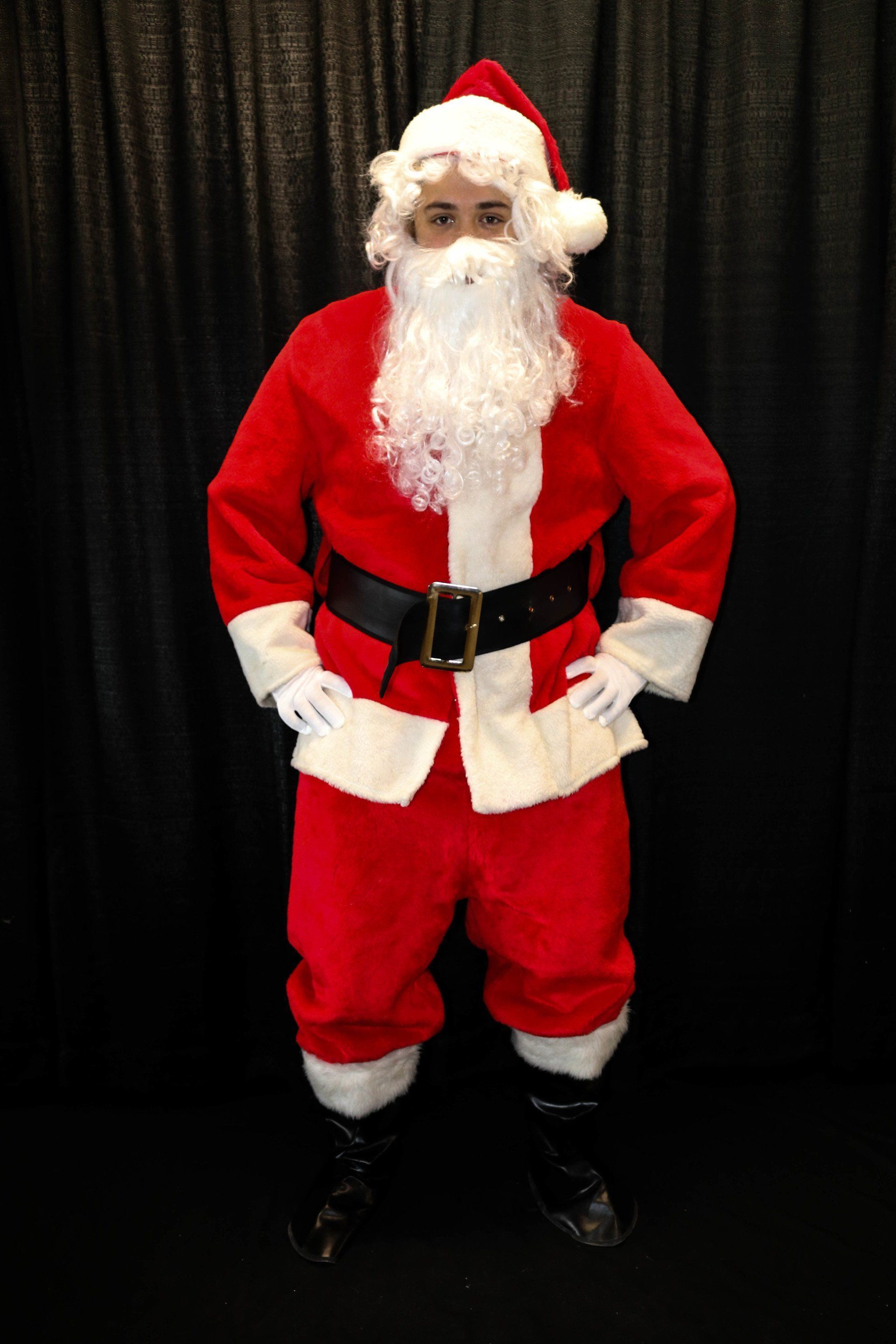 A man in a santa claus costume is standing with his hands on his hips.