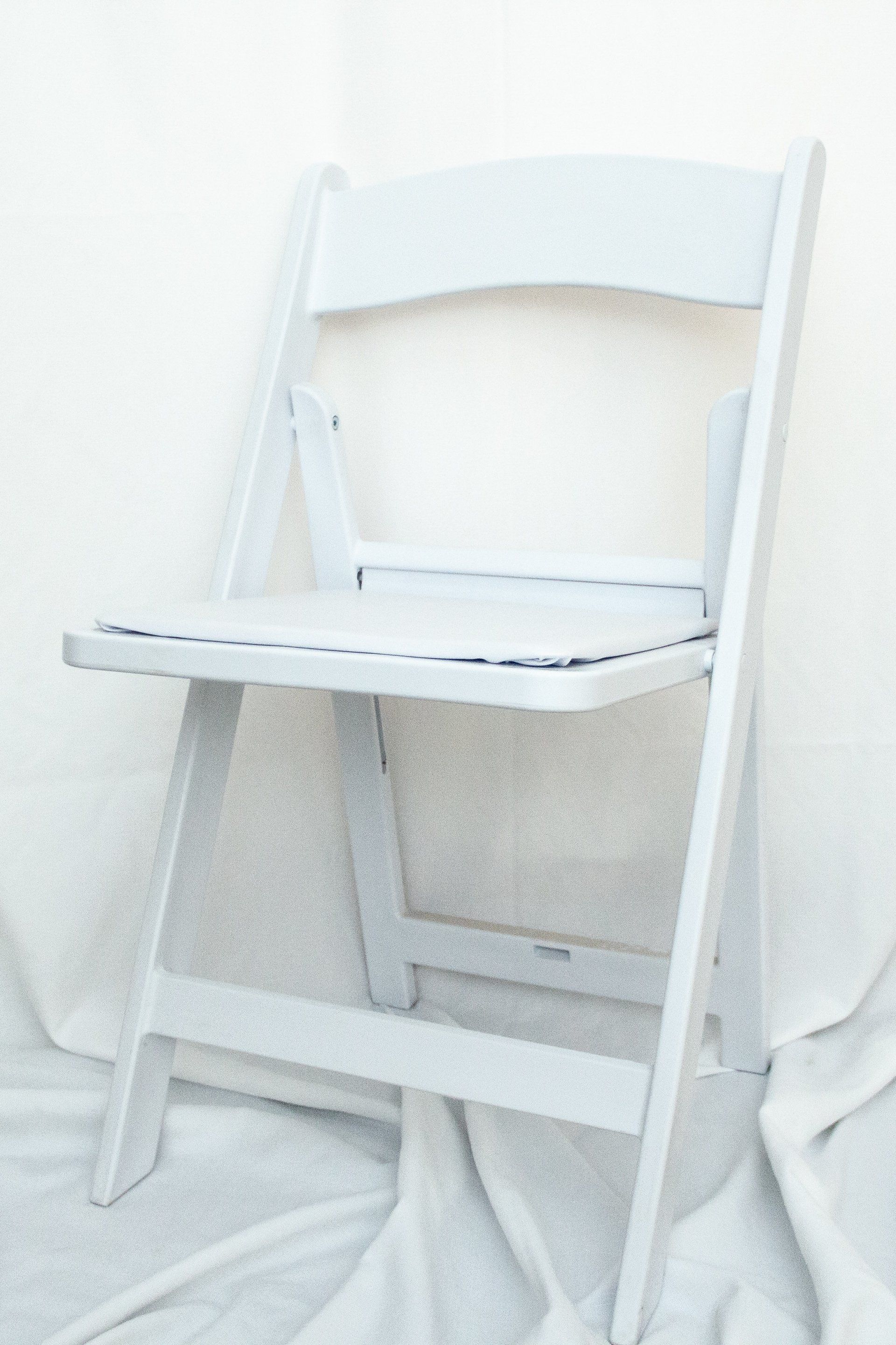 A white folding chair is sitting on a white cloth